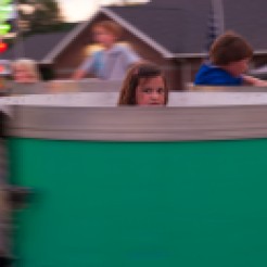 A young girl watches her family as she rides the teacups.